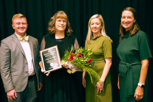 From left Andy Paul, Cindy Meadows, Lindsey Bridges and Melanie Biersmith smile together. Cindy Meadows holds a plaque and bouquet of flowers.