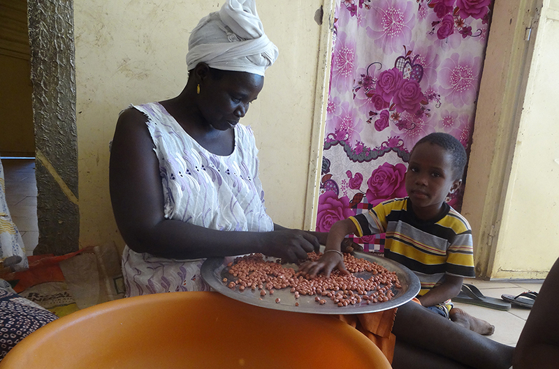 A woman sorts groundnuts while caring for a child.