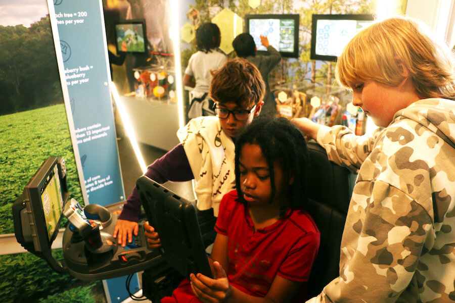 Three fourth grade students view a screen for a virtual peanut tractor