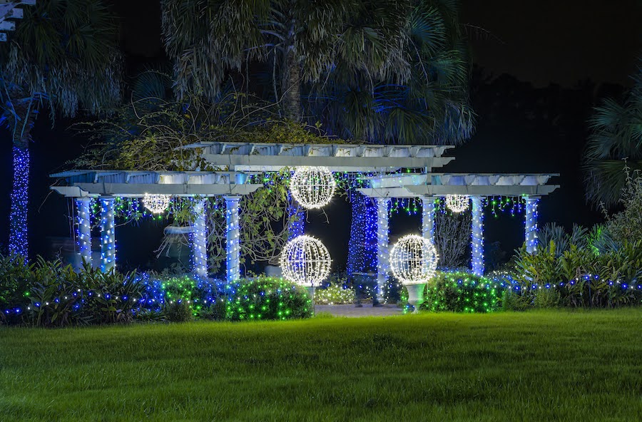 Multicolored holiday lights cover a pavilion with palm trees in the background