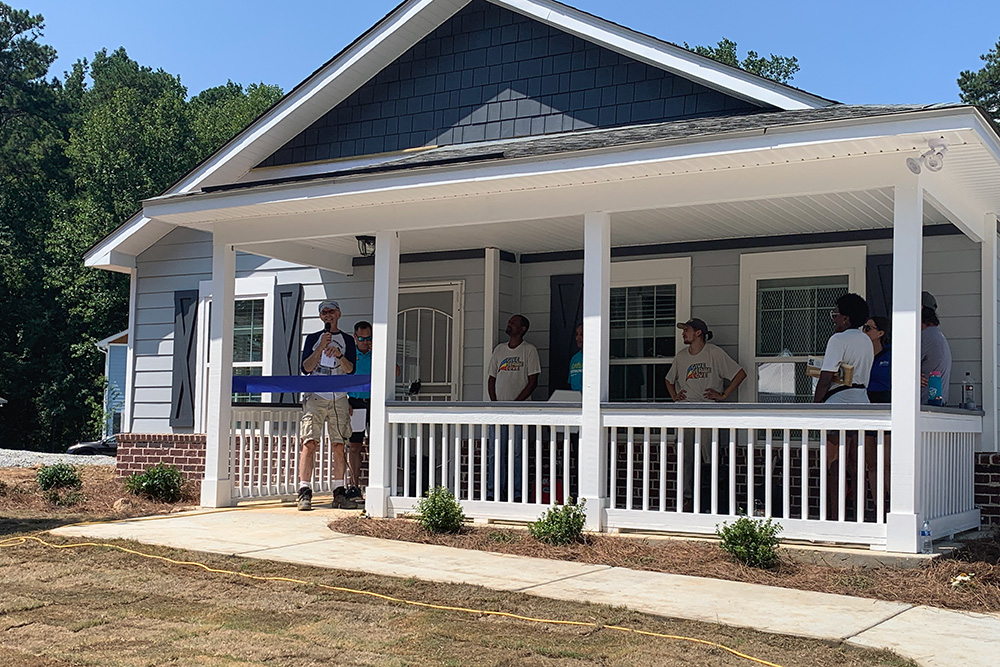 A group of people stand on the front porch of a Habitat for Humanity home.