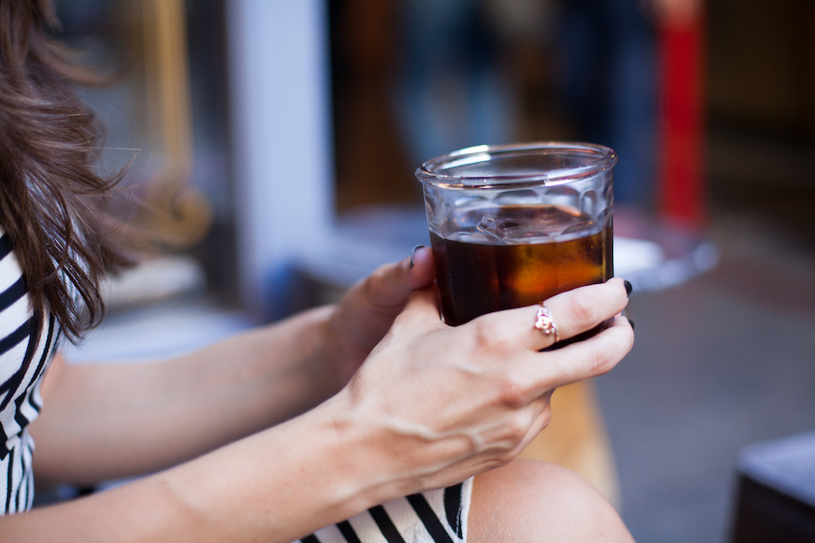 Woman sits outside drinking cold brew coffee in a glass