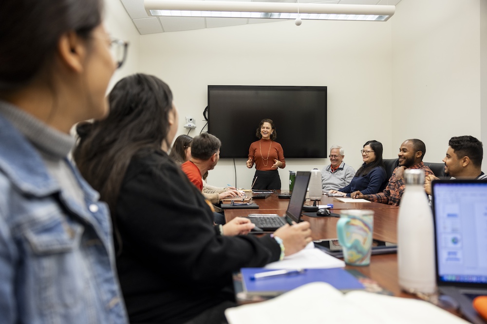 Soraya Leal-Bertioli stands at the front of a classroom leading a conversation with students and faculty seated around a long table