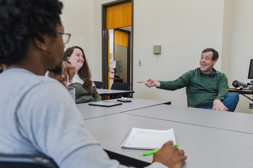 Chris Rhodes smiles and points at a student in the CIT Program seated with others in her cohort