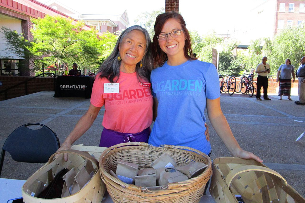 Two smiling women stand at a market table with baskets of tea in front of them.