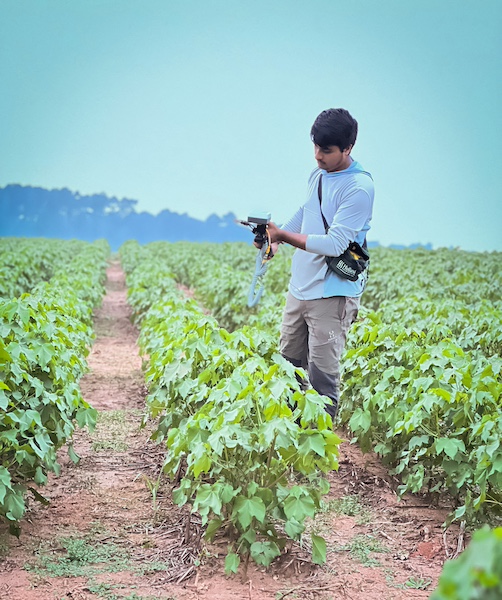 Anish Bhattarai stands and examines agricultural technology equipment in a field setting