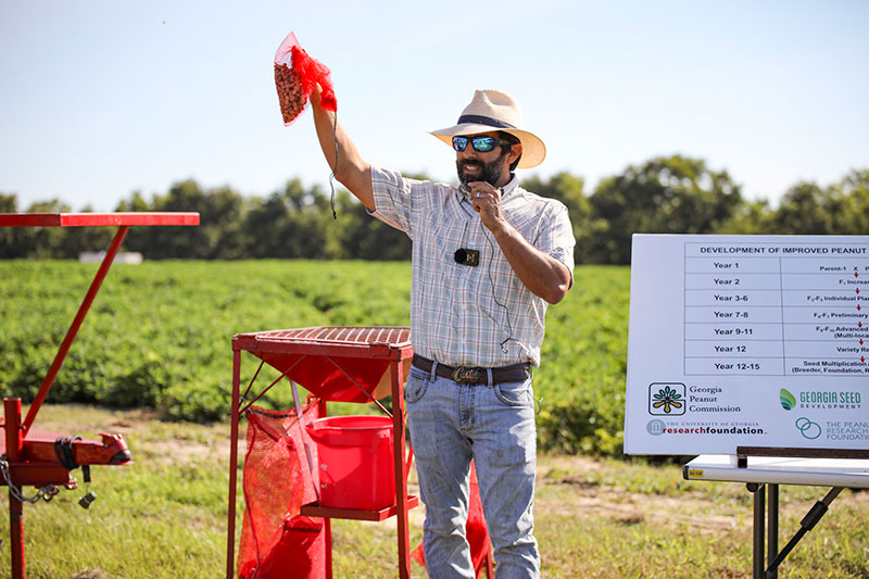 Nino Brown stands in front of a peanut field holding up a red net bag of harvested peanuts above his head as he speaks to participants in the Georgia Peanut Tour in 2022.