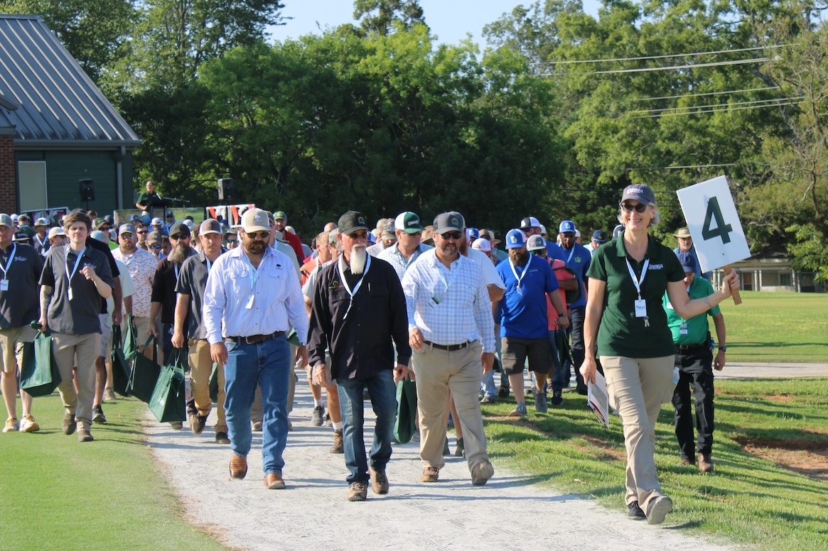 A UGA researcher holding a sign reading "4" leads a large crowd to a presentation station