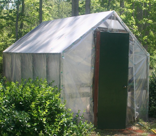 A 10-by-14 structural frame greenhouse built with treated wood and commercial-grade plastic.