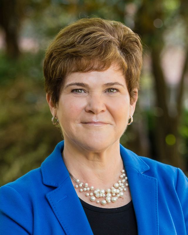 headshot photo of a woman with short brown hair wearing a blue blazer and a pearl necklace